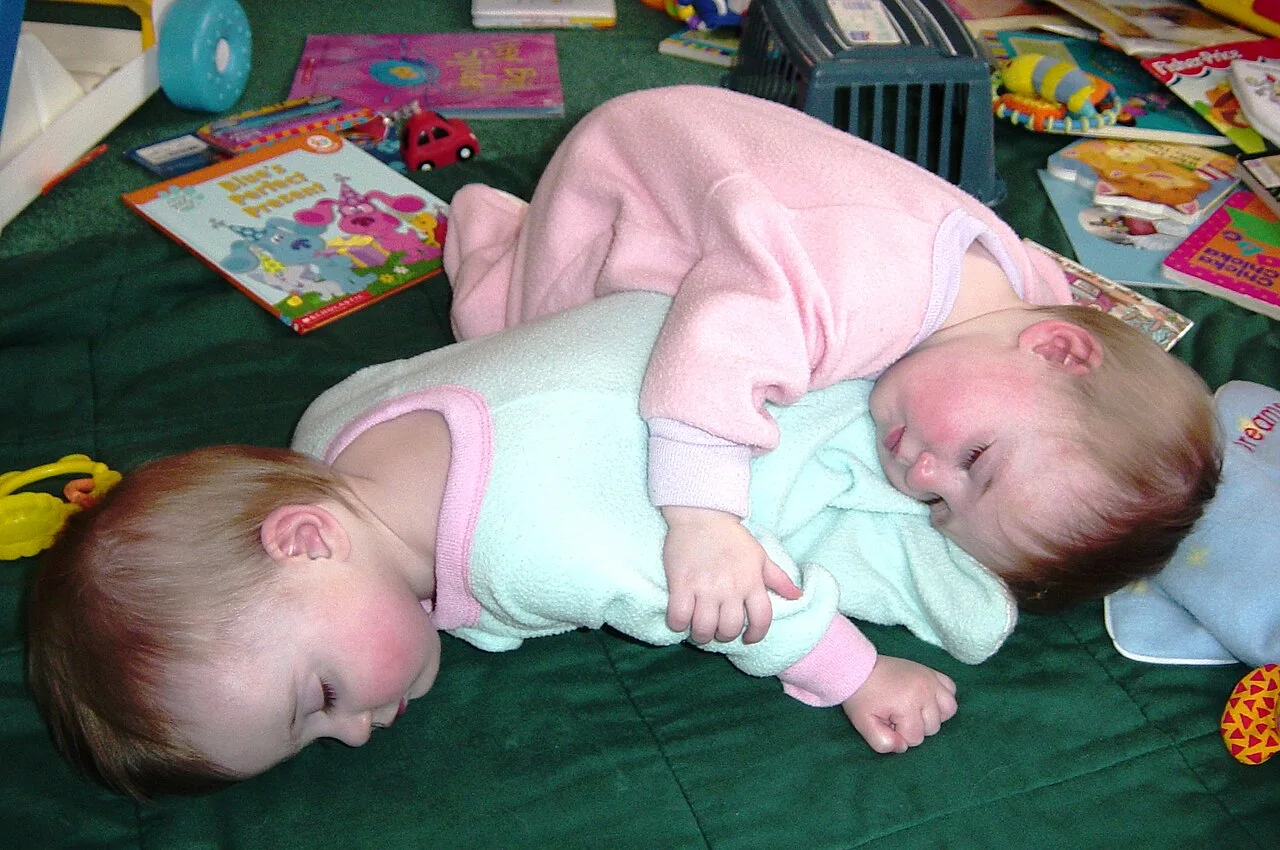 Photograph of eight month old fraternal twinen sisters napping together.
